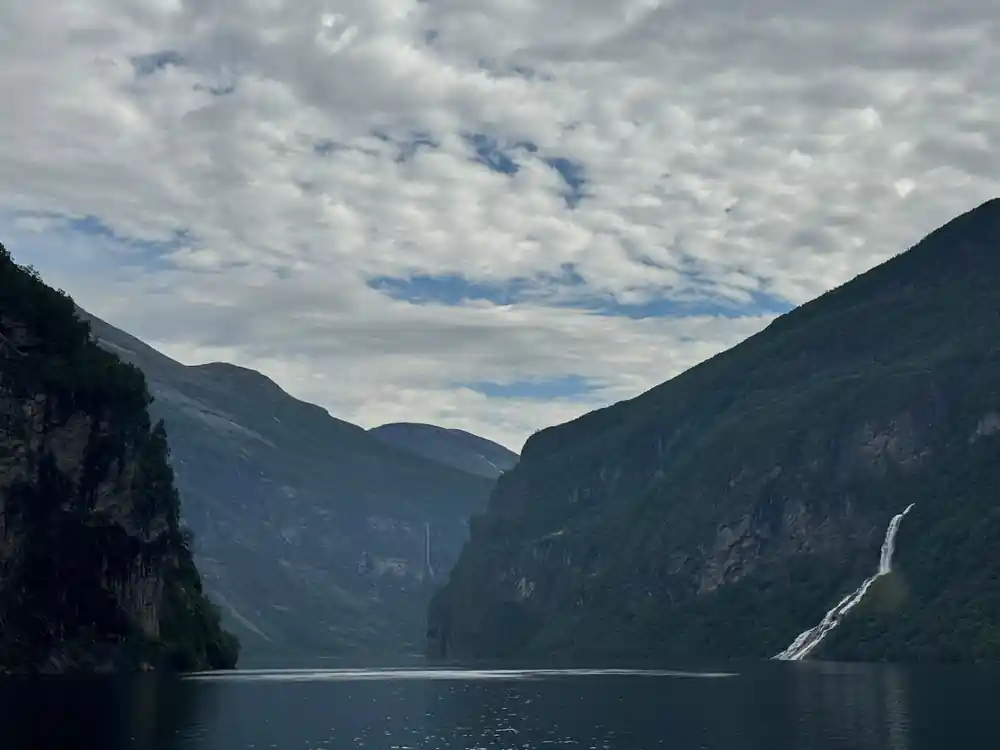 Deep fjord valley with mountains and waterfall visible ahead