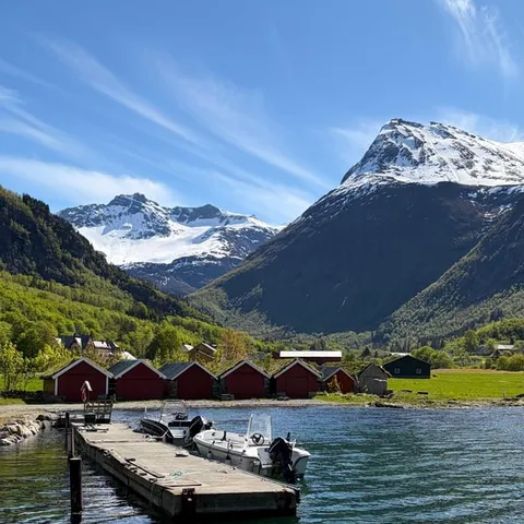 Red boathouses and a pier on the Hjørundfjord below snowy peaks