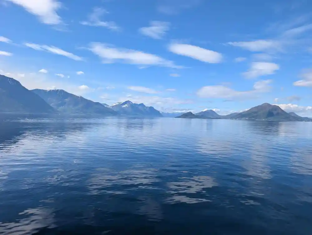 Mirror-calm blue water reflecting distant snow mountains