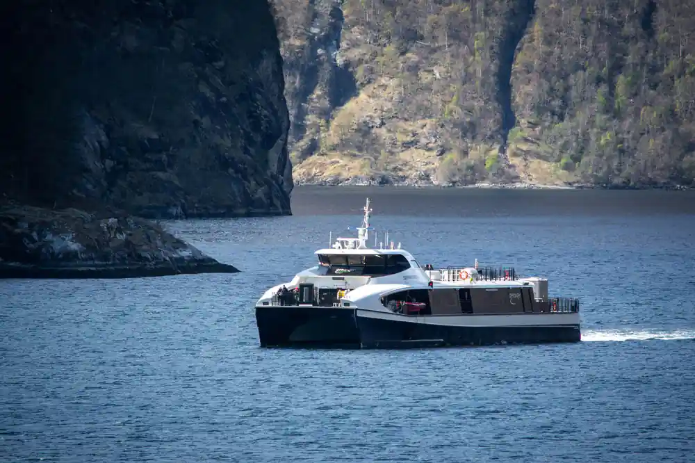 Modern ferry boat on water between dark cliffs