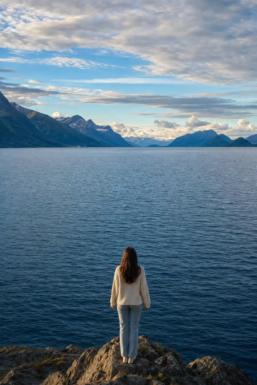 Mountain range across calm water with white clouds