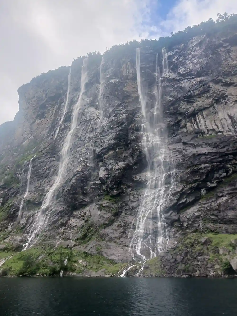 Multiple thin waterfalls cascading down dark cliff to fjord