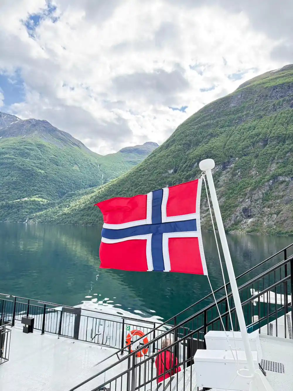 Norwegian flag on boat with green fjord mountains