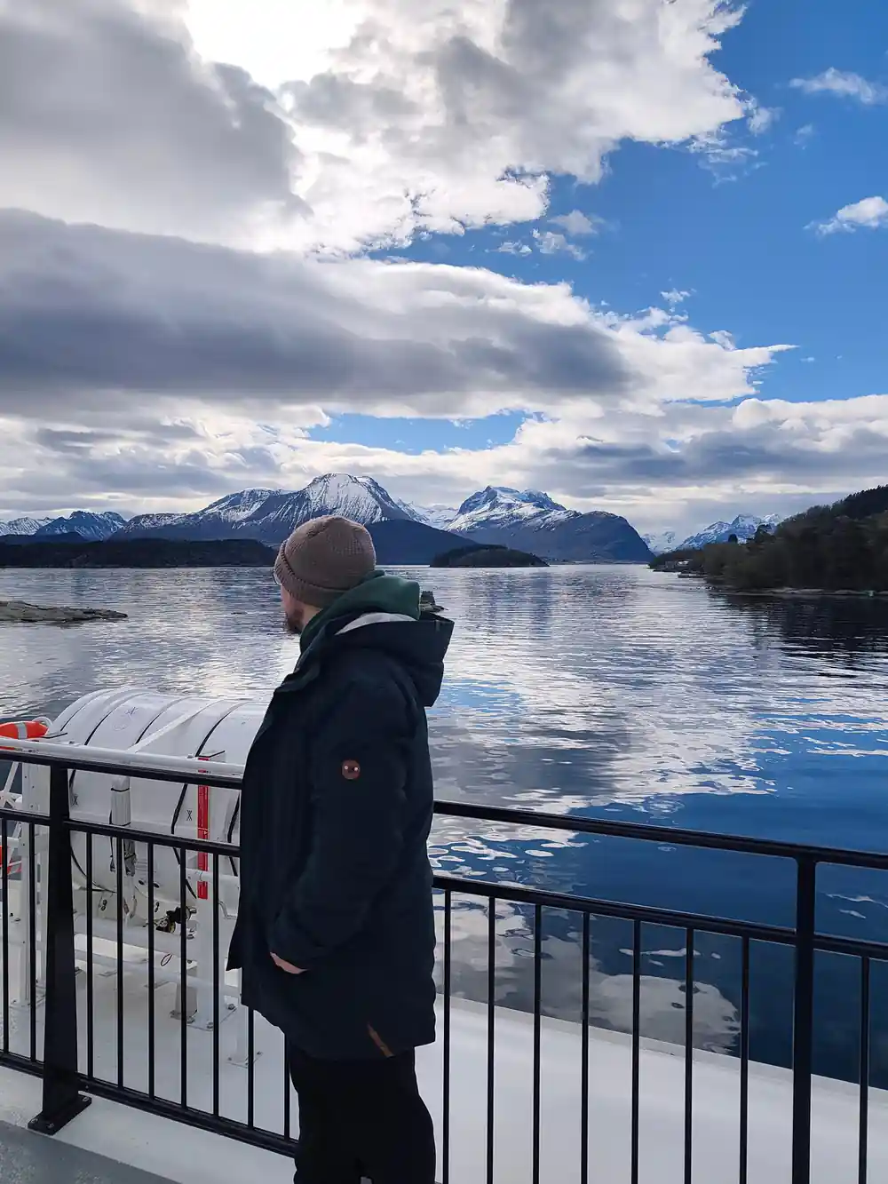 Person on boat deck viewing snow-capped mountains