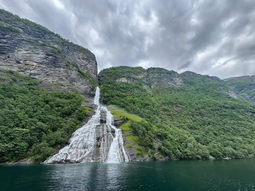 Steep waterfall on cliff face above still fjord water