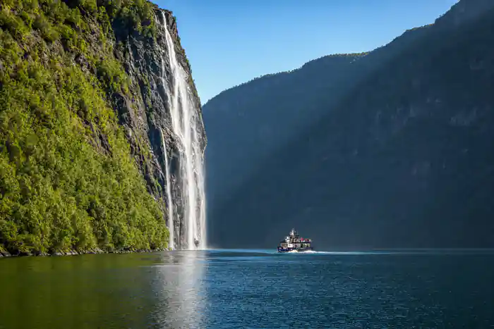 Tall waterfall flowing down cliff beside boat