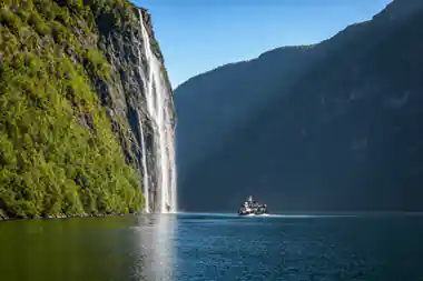 Tall waterfall flowing down cliff beside boat