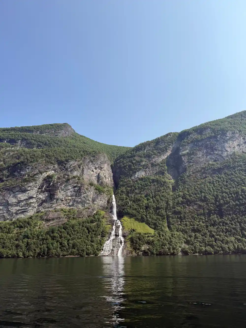 Thin waterfall streaming down cliff into dark water