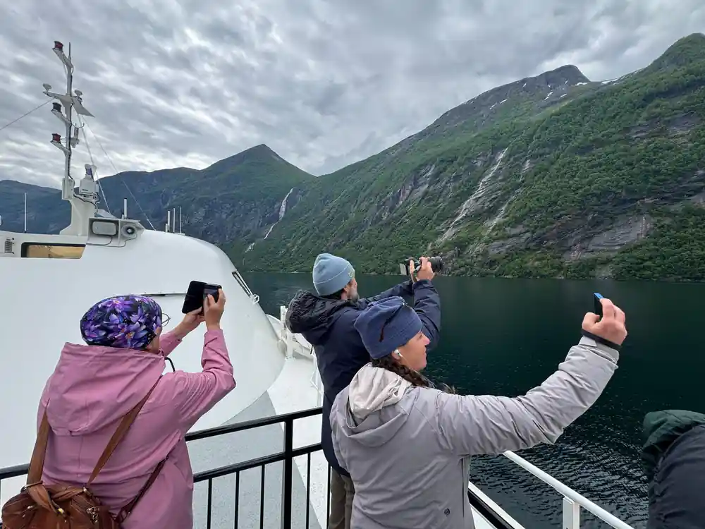 Tourists on boat deck photographing mountains and fjord scenery