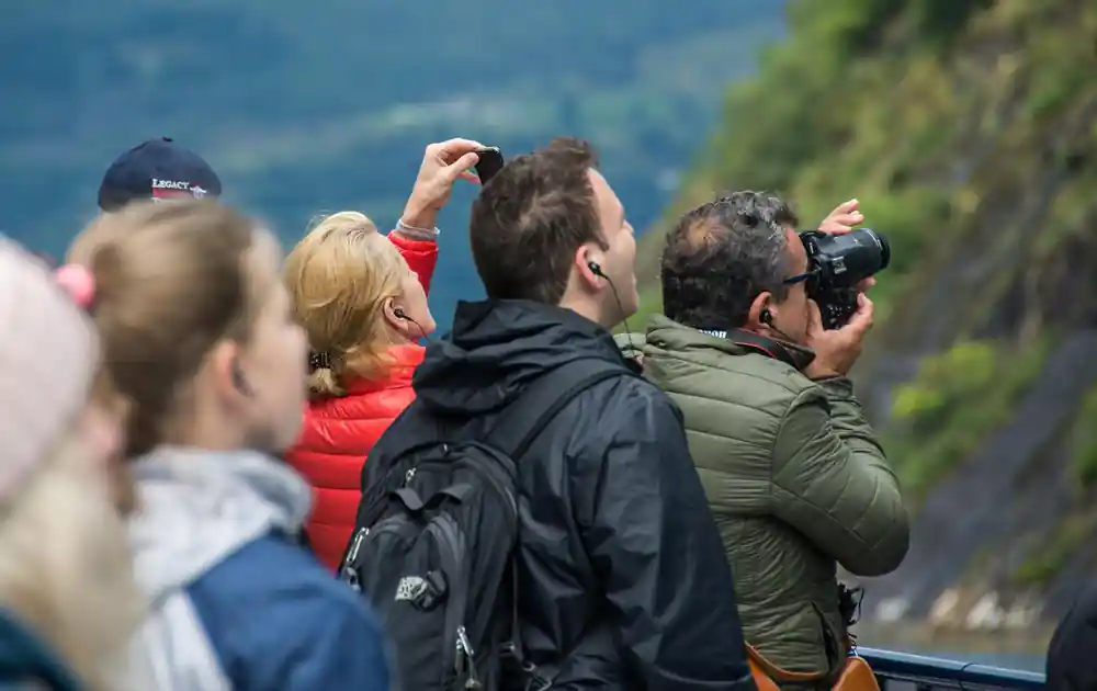 Tourists photographing scenic fjord landscape from deck