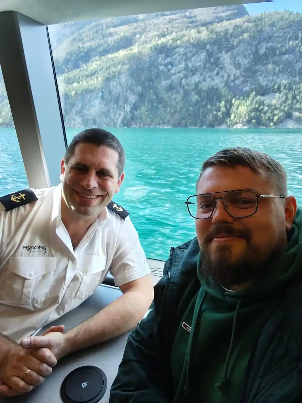Two men smiling inside boat with turquoise lake