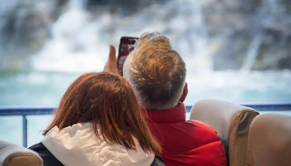 Two people on boat taking photo of waterfall