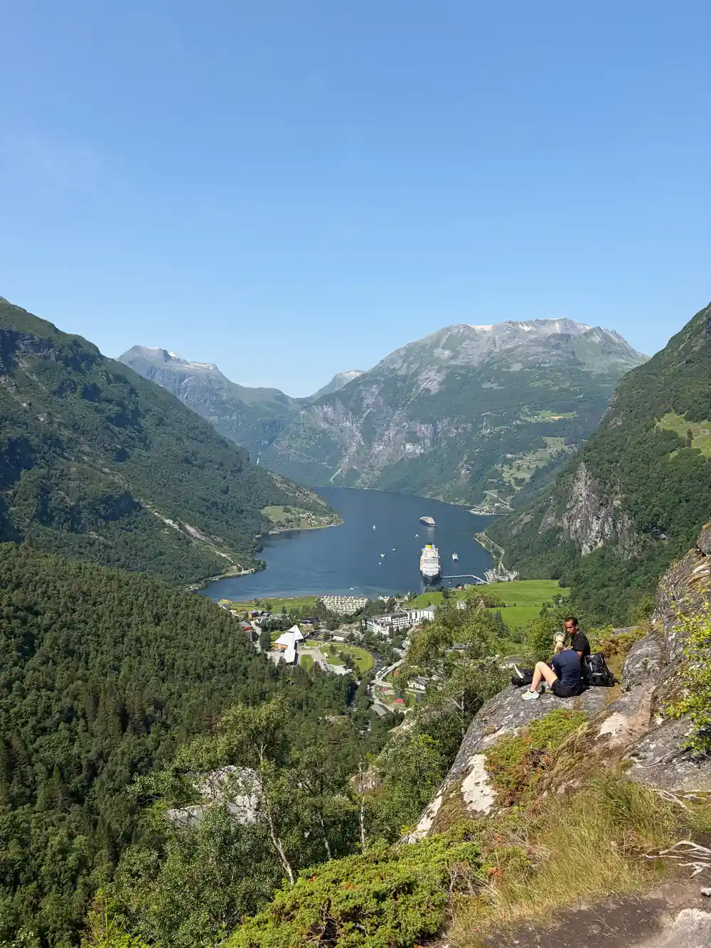 Two people sitting on mountain overlook above fjord and village