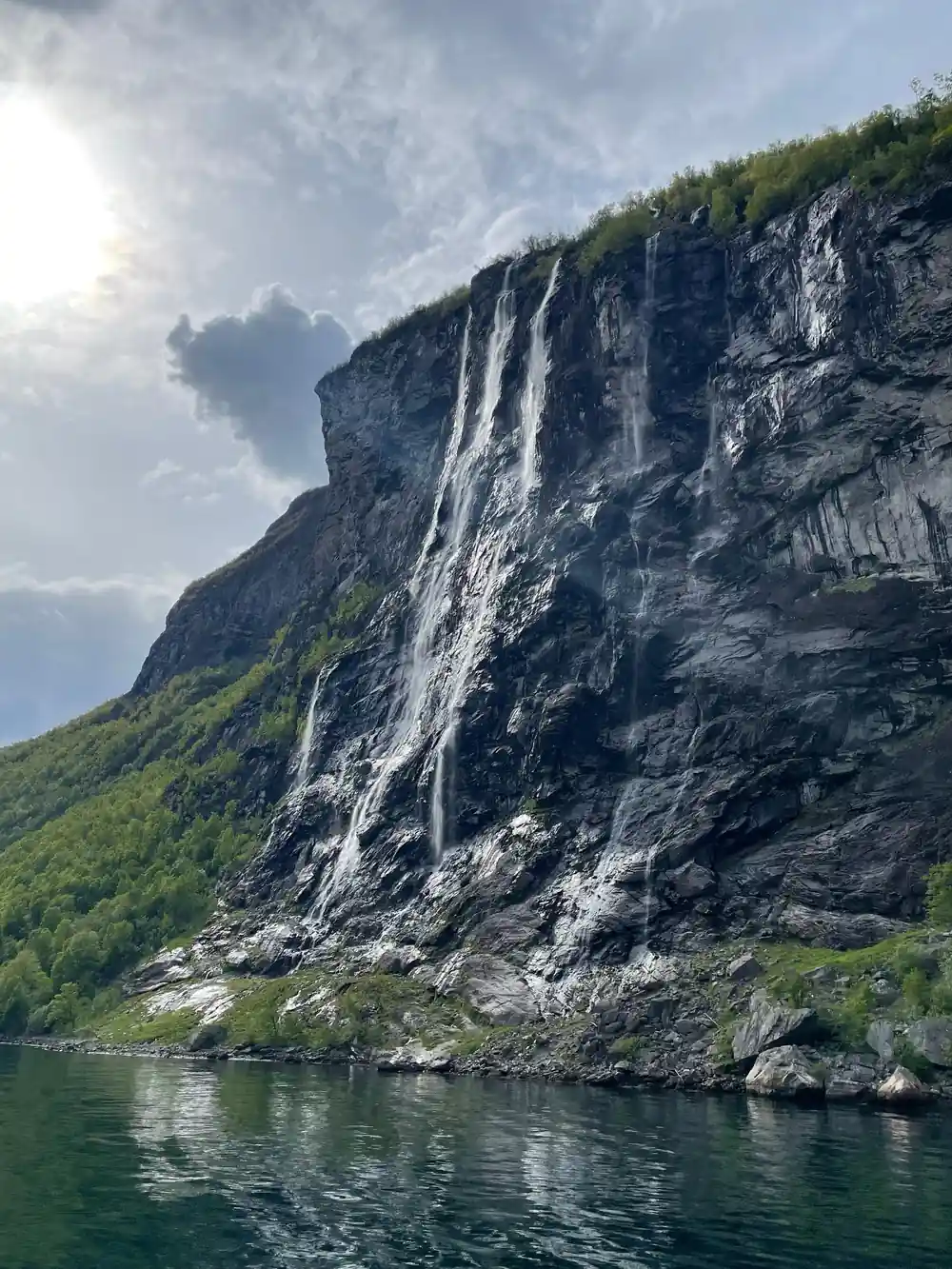 Waterfall cascading down steep cliff into green fjord water