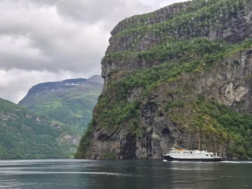 White ship passing tall cliff face in narrow fjord