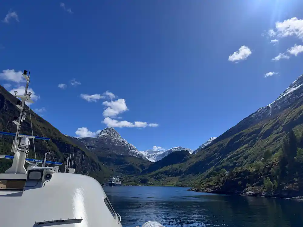 White tour boat beneath tall mountain cliff with waterfall
