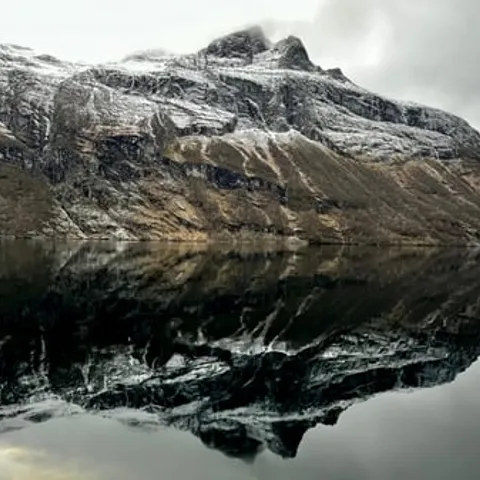 Snow-dusted mountains mirrored in the still fjord in winter